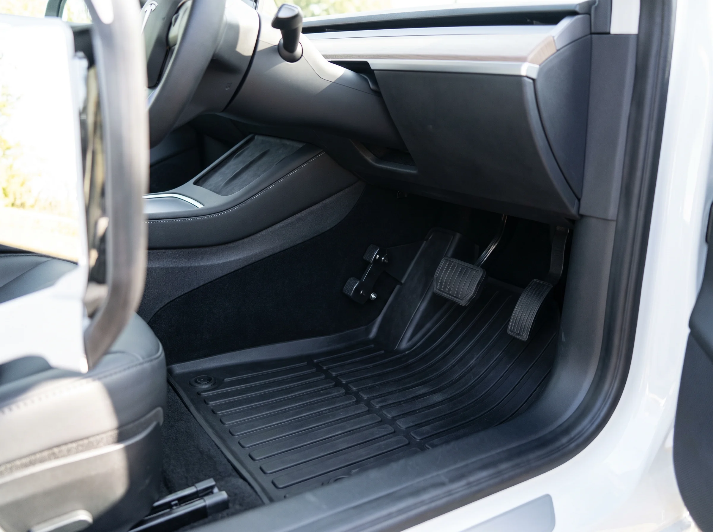 Clean modern learner-car instructor footwell with dual-control pedals and a new black rubber mat.